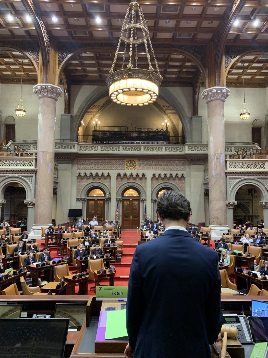 A delegate at the podium facing the New York State Assembly chamber